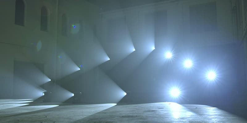 Multiple Claypaky Arolla Aqua fixtures fanning sharp blue beams through haze in a large hall